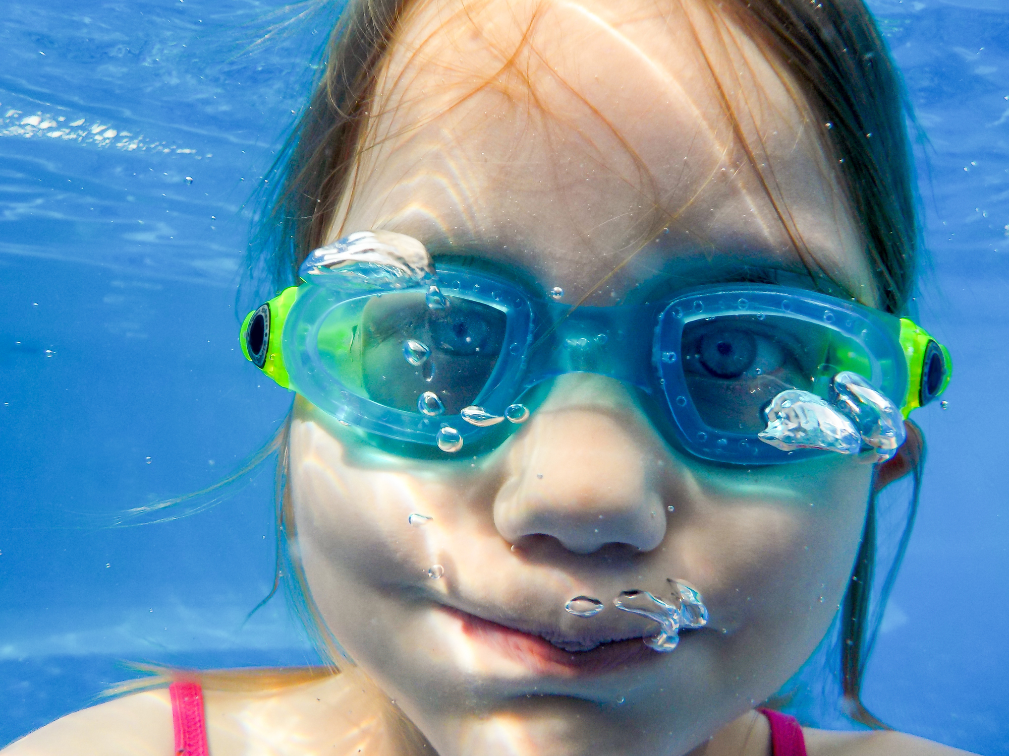 A girl with diving goggles dives in the pool and holds her breath