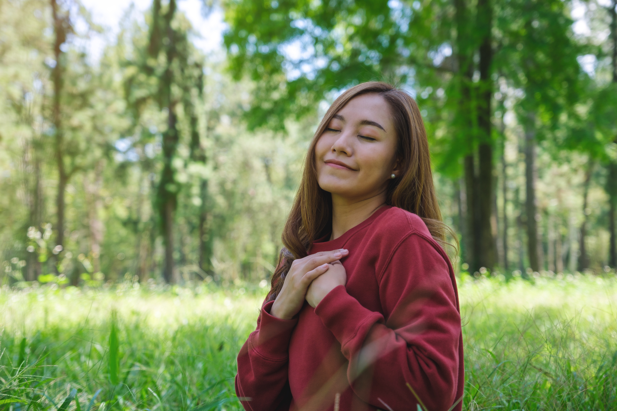 Portrait image of a young woman with closed eyes putting hands on her chest in the park